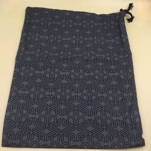 May include: A dark gray drawstring bag with a geometric pattern. The pattern is made up of repeating shapes that resemble the letter "A".