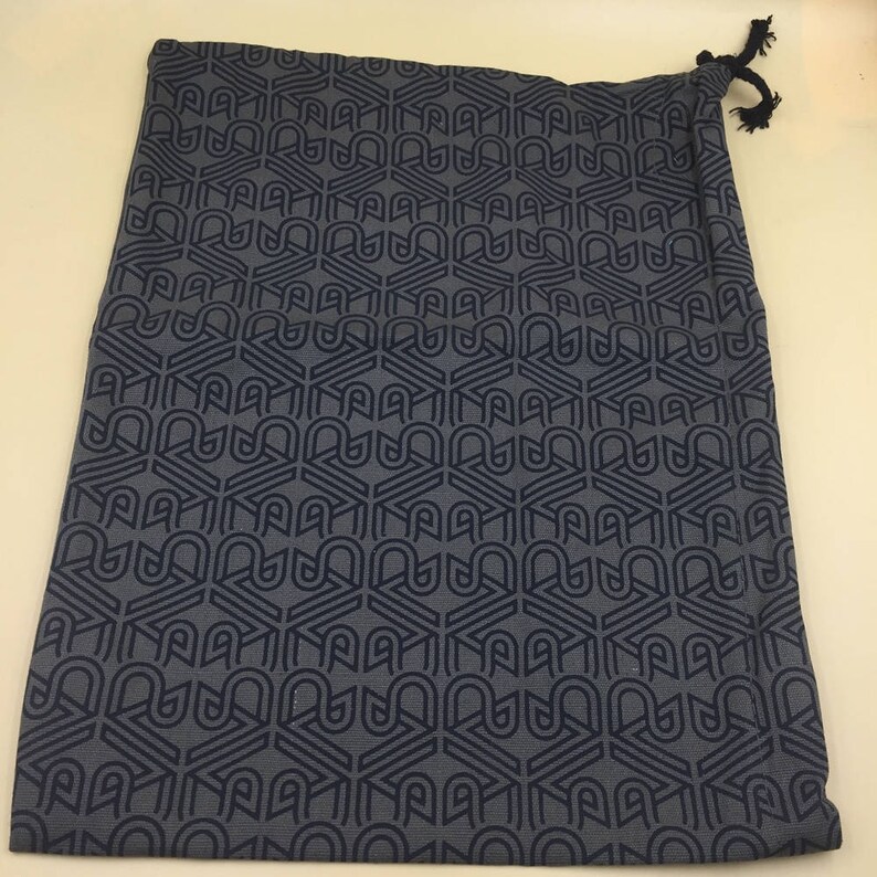 May include: A dark gray drawstring bag with a geometric pattern. The pattern is made up of repeating shapes that resemble the letter "A".