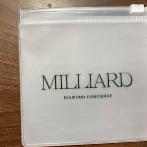 May include: A clear plastic zippered pouch with the word "MILLIARD" in green, and the text "DIAMOND CONCIERGE" below it. The pouch is rectangular and has a white zipper.