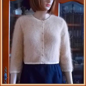 Peut inclure: Un cardigan beige clair et doux avec un devant boutonné. Le cardigan est fait d'un matériau duveteux ressemblant à du mohair et a une longueur courte.