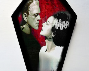 May include: A black and white illustration of Frankenstein's monster and his bride, with a red background. The image is in a coffin shape and has the text "@LALAS ART" at the bottom.