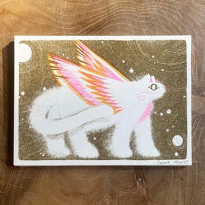 May include: An illustration of a white winged creature with pink and orange wings, set against a gold background with stars and moons. The artwork is signed "Carole Mariet" in the lower right corner.