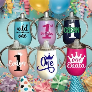 May include: Six personalized stainless steel sippy cups with different designs and names. The cups are blue, purple, pink, white, and red. The designs include a crown, a number one, and the words "wild one", "1st birthday", "Casen", "Eolyn", "One", and "Evata".