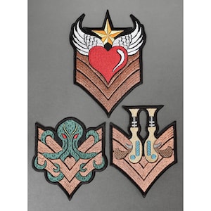 May include: Three embroidered patches with different designs. The first patch is brown with a gold star and wings, a red heart, and the text "Love". The second patch is brown with a green octopus. The third patch is brown with two blue and white musical notes.