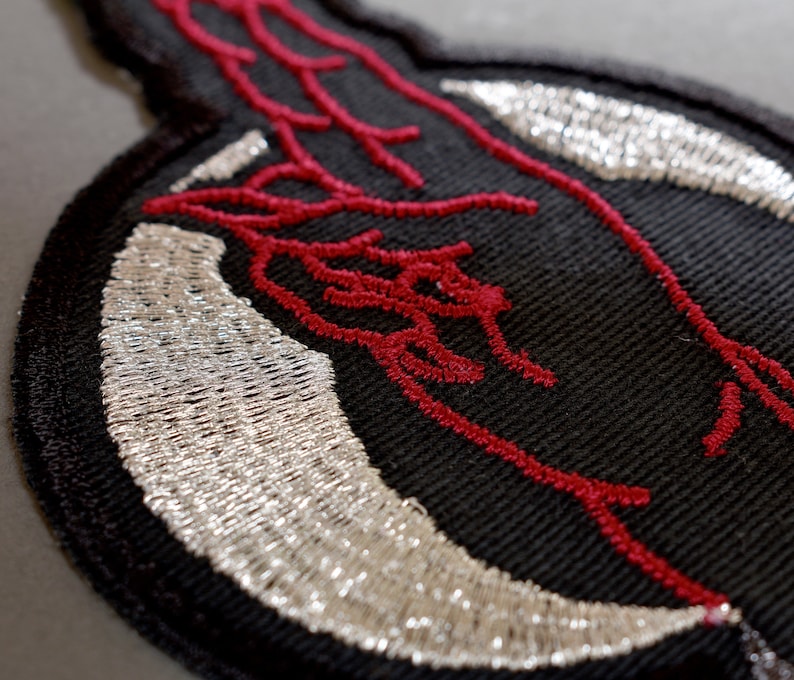May include: Black embroidered patch with a red design of a hand with a silver crescent moon.