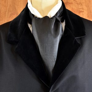 Puede incluir: Una chaqueta negra con ribete de terciopelo, una corbata de satén negro y un botón decorativo.