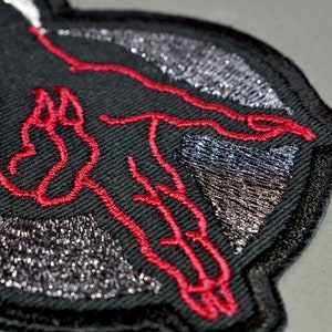 May include: Black embroidered patch with a red outline of a hand reaching out. The patch has a silver glitter design.