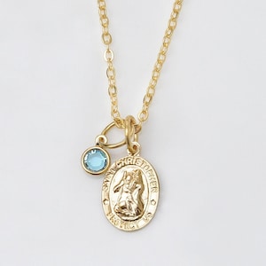 Puede incluir: Collar de cadena dorada con un pequeño dije de piedra azul y un dije ovalado dorado con la inscripción "San Cristóbal Protégenos".