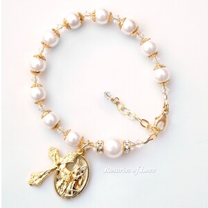 Op de afbeelding: Wit parel en kristal rozenkrans armband met een gouden engel en kruis bedel. De armband heeft een gouden sluiting en is versierd met heldere kristallen.
