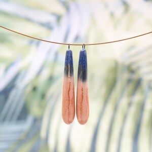 Op de afbeelding: Een paar handgemaakte oorbellen met een uniek ontwerp. De oorbellen zijn lang en druppelvormig, met een kleurovergang. De bovenkant van elke oorbel is donkerblauw, vervaagt naar zwart en vervolgens naar een licht oranje-bruine kleur.