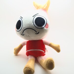 以下が含まれることがあります： 白い頭、大きな黒い目、しかめっ面をしたぬいぐるみ。赤い胴体、ベージュの腕と脚、頭のてっぺんには黄色のひれのようなディテールがあります。おもちゃは直立するように設計されています。