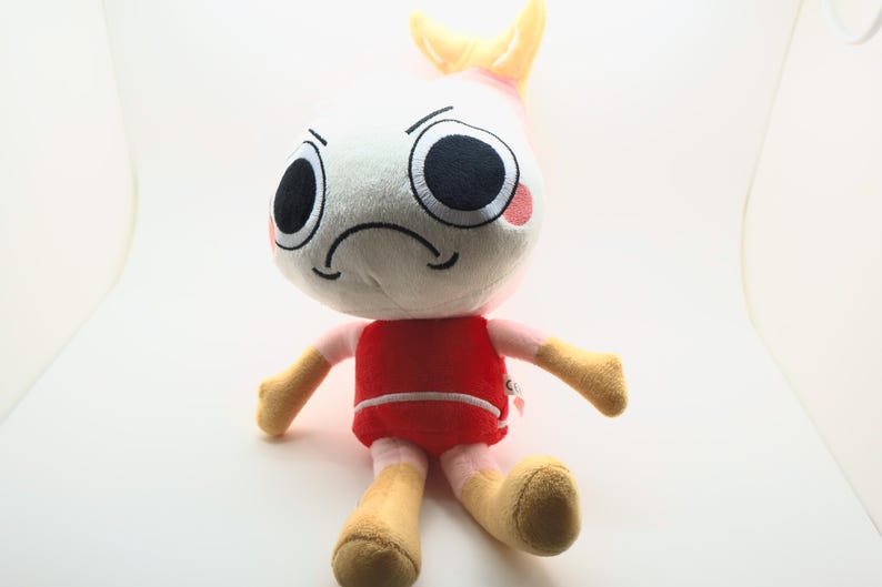 以下が含まれることがあります： 白い頭、大きな黒い目、しかめっ面をしたぬいぐるみ。赤い胴体、ベージュの腕と脚、頭のてっぺんには黄色のひれのようなディテールがあります。おもちゃは直立するように設計されています。