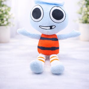 May include: A soft toy character with a light blue head and arms, large black eyes, and a smiling mouth. The body is orange with black stripes, and the legs are blue with white and orange striped socks. The toy is designed to be cuddly.