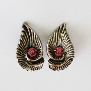 Puede incluir: Un par de pendientes de plata con una pedrería rosa en el centro de cada pendiente. Los pendientes tienen forma de lágrima con un diseño de abanico.