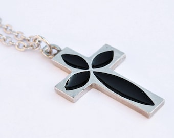 May include: A silver chain necklace with a silver cross pendant. The cross has a black enamel design of a stylized flower.