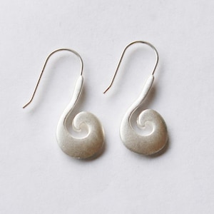 May include: A pair of silver earrings with a swirl design. The earrings are made of brushed metal and have a simple, elegant look.