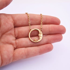 Può includere: Collana d'oro con un ciondolo a forma di luna crescente con un viso e una piccola stella all'interno della luna.