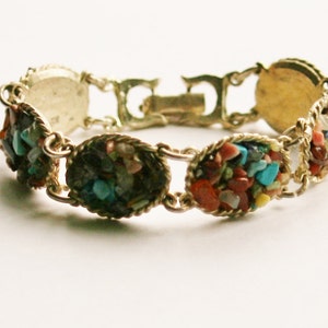 May include: A gold bracelet with a series of oval-shaped links, each filled with colorful, small, irregular stones. The stones are a mix of red, orange, yellow, blue, green, and brown.