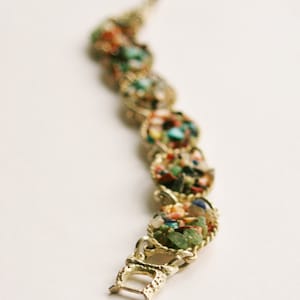 May include: A gold bracelet with a clasp closure. The bracelet is made of small, colorful stones set in gold.