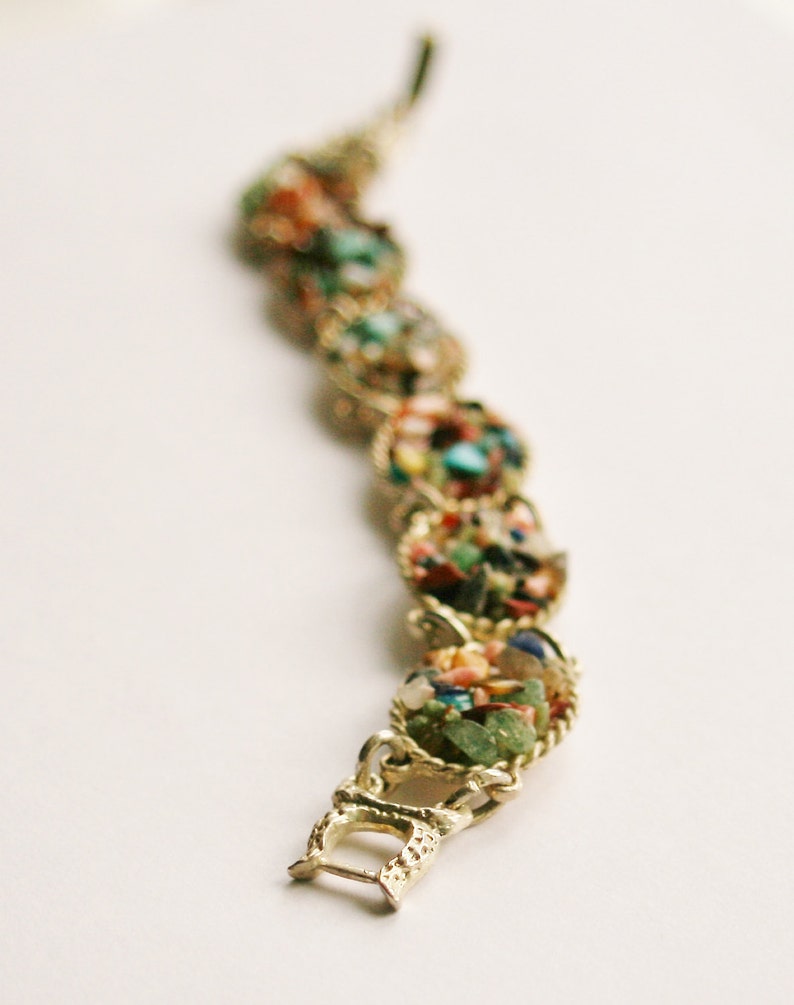 May include: A gold bracelet with a clasp closure. The bracelet is made of small, colorful stones set in gold.