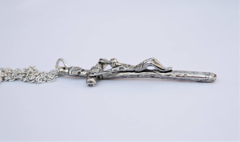 May include: A silver chain necklace with a silver crucifix pendant. The crucifix features a figure of Jesus Christ on a wooden cross.