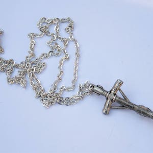 May include: A silver chain necklace with a silver cross pendant. The cross is detailed with a textured design.