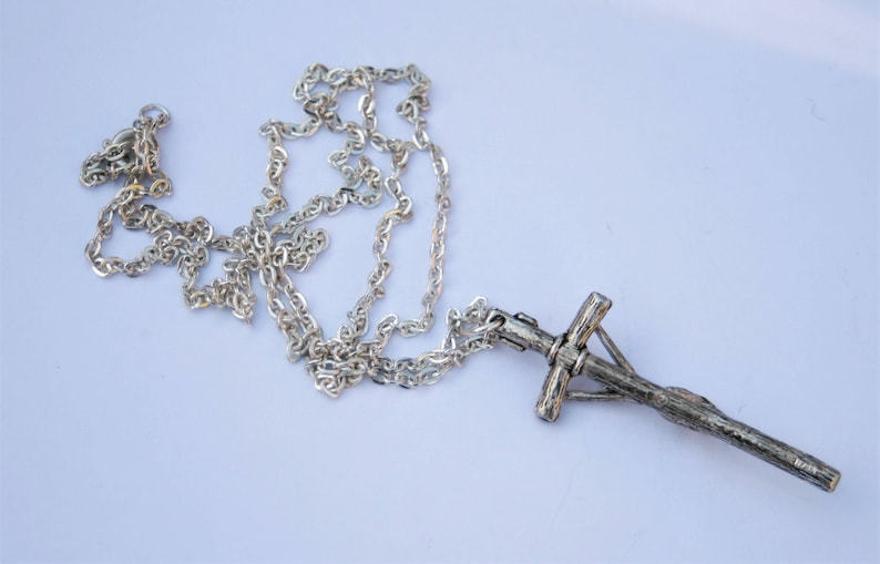 May include: A silver chain necklace with a silver cross pendant. The cross is detailed with a textured design.