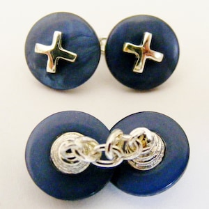Puede incluir: Un par de gemelos con fondo azul oscuro y un diseño de cruz dorada. Los gemelos están conectados por una cadena plateada.