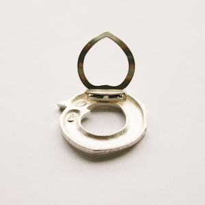 May include: Silver ring with a hinged opening, the ring is in the shape of a circle with a textured surface. The ring is open and the hinge is visible.