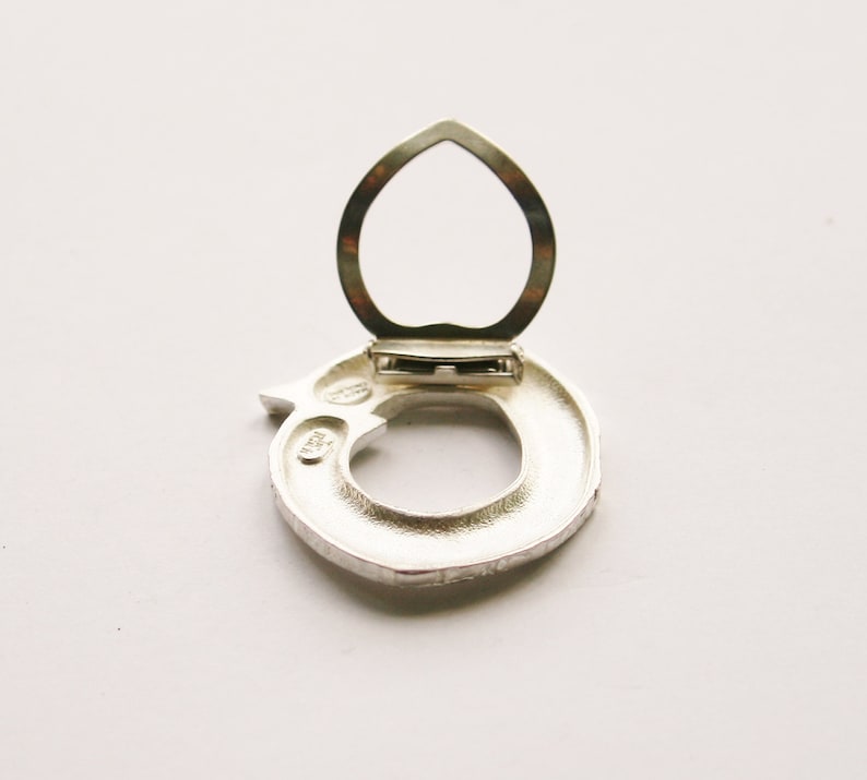 May include: Silver ring with a hinged opening, the ring is in the shape of a circle with a textured surface. The ring is open and the hinge is visible.