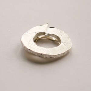 May include: A silver ring with a textured, organic shape. The ring is open and has a circular opening.