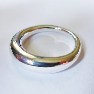 Pode incluir: Um anel de prata liso com um design arredondado e curvo. O anel é polido e brilhante.