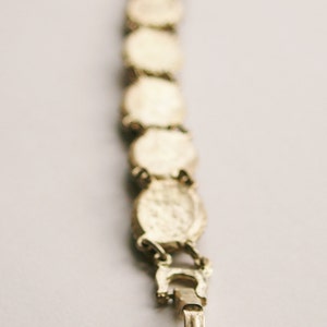May include: A gold-toned bracelet with a chain link design and a clasp closure. The bracelet is made up of a series of round, decorative links.