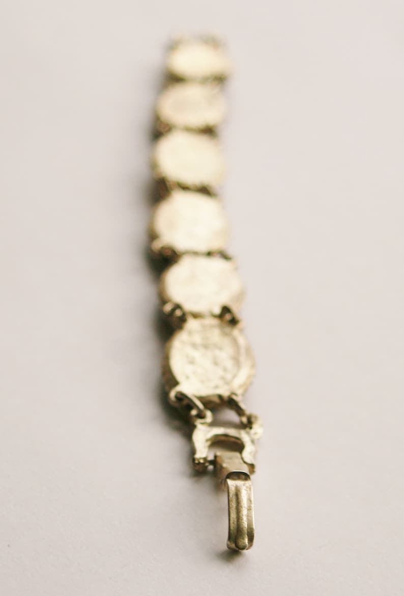 May include: A gold-toned bracelet with a chain link design and a clasp closure. The bracelet is made up of a series of round, decorative links.