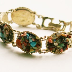 May include: A gold bracelet with a variety of colorful stones set in oval shapes. The stones are a mix of turquoise, blue, green, red, and white.