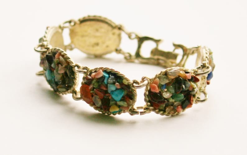 May include: A gold bracelet with a variety of colorful stones set in oval shapes. The stones are a mix of turquoise, blue, green, red, and white.