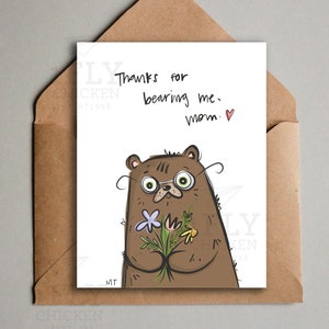 Peut inclure: Carte de v&oelig;ux avec une illustration d'ours brun tenant des fleurs. Le texte manuscrit dit : &laquo; Merci de m'avoir support&eacute;, maman &raquo;. La carte est dans une enveloppe marron. L'ours a de grands yeux et est dessin&eacute; dans un style fantaisiste.