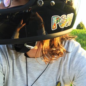 K&ouml;nnte beinhalten: Eine Person tr&auml;gt einen schwarzen Motorradhelm mit einem bunten Aufkleber, auf dem "PGH" steht. Die Person tr&auml;gt auch einen grauen Pullover mit einer schwarzen Halskette und einem schwarzen Knopf, auf dem "Black Lives Matter" steht.