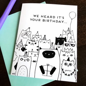 May include: A black and white greeting card with a group of cats wearing party hats and holding a gift. The card reads "We heard it's your birthday..."