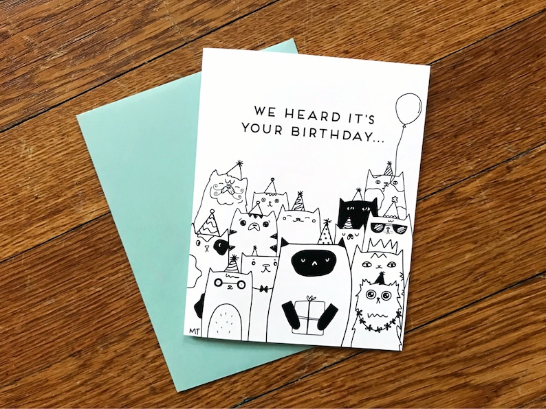 May include: A birthday card with a black and white illustration of a group of cats wearing party hats and holding a gift. The text on the card reads "We heard it's your birthday..."