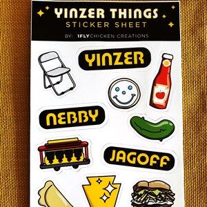 K&ouml;nnte beinhalten: Eine Sticker-Tafel mit verschiedenen Designs zum Thema Pittsburgh, darunter ein Klappstuhl, ein Smiley, eine Ketchupflasche, eine Gurke, eine Stra&szlig;enbahn, ein Pierogi, der Bundesstaat Pennsylvania und ein Sandwich. Die Tafel enth&auml;lt auch den Text "Yinzer Things" und "1flychicken.com".