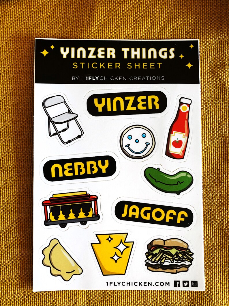 K&ouml;nnte beinhalten: Eine Sticker-Tafel mit verschiedenen Designs zum Thema Pittsburgh, darunter ein Klappstuhl, ein Smiley, eine Ketchupflasche, eine Gurke, eine Stra&szlig;enbahn, ein Sandwich, ein Pierogi und der Bundesstaat Pennsylvania. Die Tafel enth&auml;lt auch den Text "Yinz" und "Jagoff".