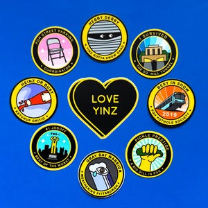 Pu&ograve; includere: Nove adesivi rotondi con contorni neri e testo giallo su sfondo blu. Gli adesivi presentano vari disegni e testi, tra cui "Love Yinz", "Heinz or Bust", "Best in Show", "Nebby Debby", "Gray Day Warrior", "Pickle Prestige", "I Survived", "PGH Street Parking" e "#1 Jagoff".