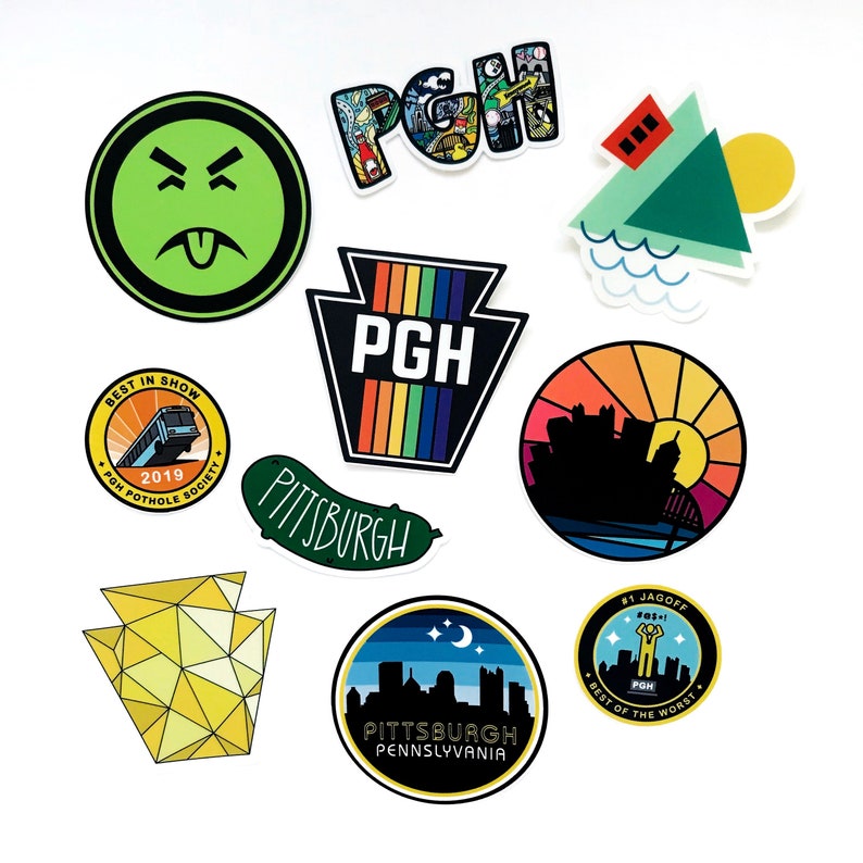 K&ouml;nnte beinhalten: Eine Sammlung bunter Aufkleber mit Motiven aus der Stadt Pittsburgh, Pennsylvania. Die Aufkleber zeigen eine gr&uuml;ne Gurke, eine gelbe geometrische Form von Pennsylvania, eine Schwarzwei&szlig;-Skyline, einen Bus, eine Regenbogen-Pennsylvania-Form, ein gr&uuml;n-gelbes Haus und ein gr&uuml;nes Gesicht mit herausgestreckter Zunge.