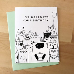 May include: A black and white birthday card with a group of cats wearing party hats and holding a gift. The card reads "We heard it's your birthday..."