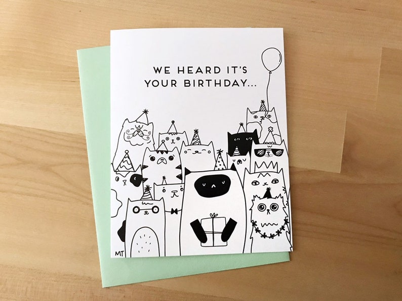 May include: A black and white birthday card with a group of cats wearing party hats and holding a gift. The card reads "We heard it's your birthday..."
