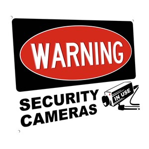 May include: A black and red warning sign with the text "WARNING" in a white oval. Below the oval is the text "SECURITY CAMERAS" in black. A black and white security camera with the text "IN USE" is in the upper right corner of the sign.