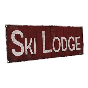 May include: A red metal sign with white lettering that reads "Ski Lodge". The sign has a distressed, vintage look.