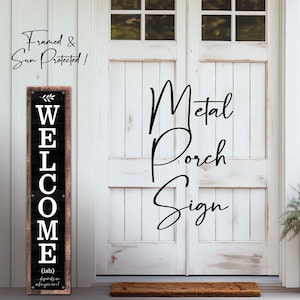 May include: Black and white metal porch sign with the word "WELCOME" in large letters. The sign is framed and has a rustic woodgrain background. The sign is hanging on a white door with a brown doormat.
