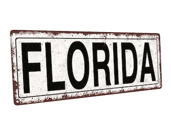 May include: A white metal sign with a rusty brown border. The sign has black text that reads "FLORIDA".